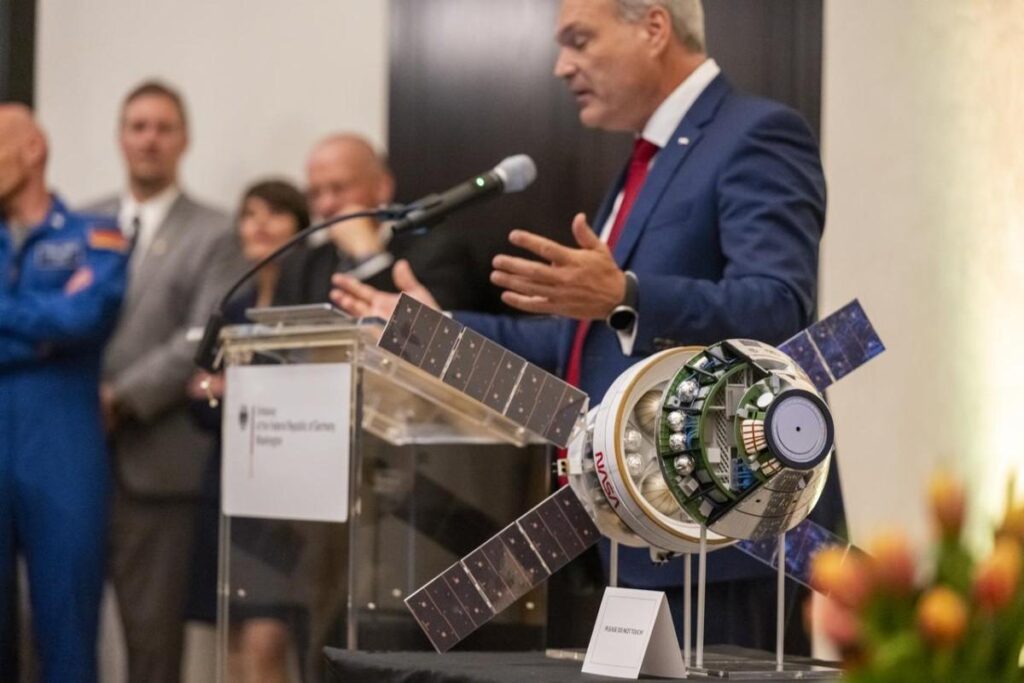 A model of the Orion Spacecraft in the foreground as Director General of the German Space Agency speaks during Artemis Accords signing ceremony