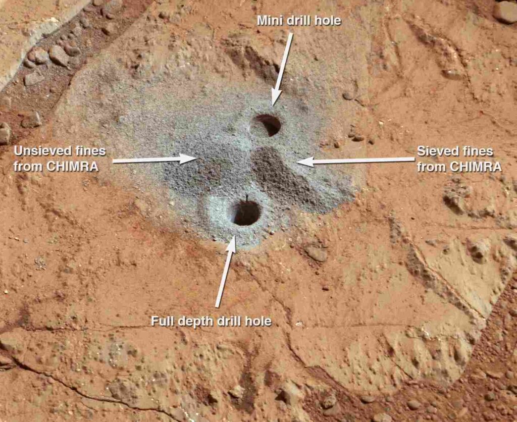 the first holes into rock drilled by NASA Mars rover Curiosity, with drill tailings around the holes plus piles of powdered rock collected from the deeper hole and later discarded.