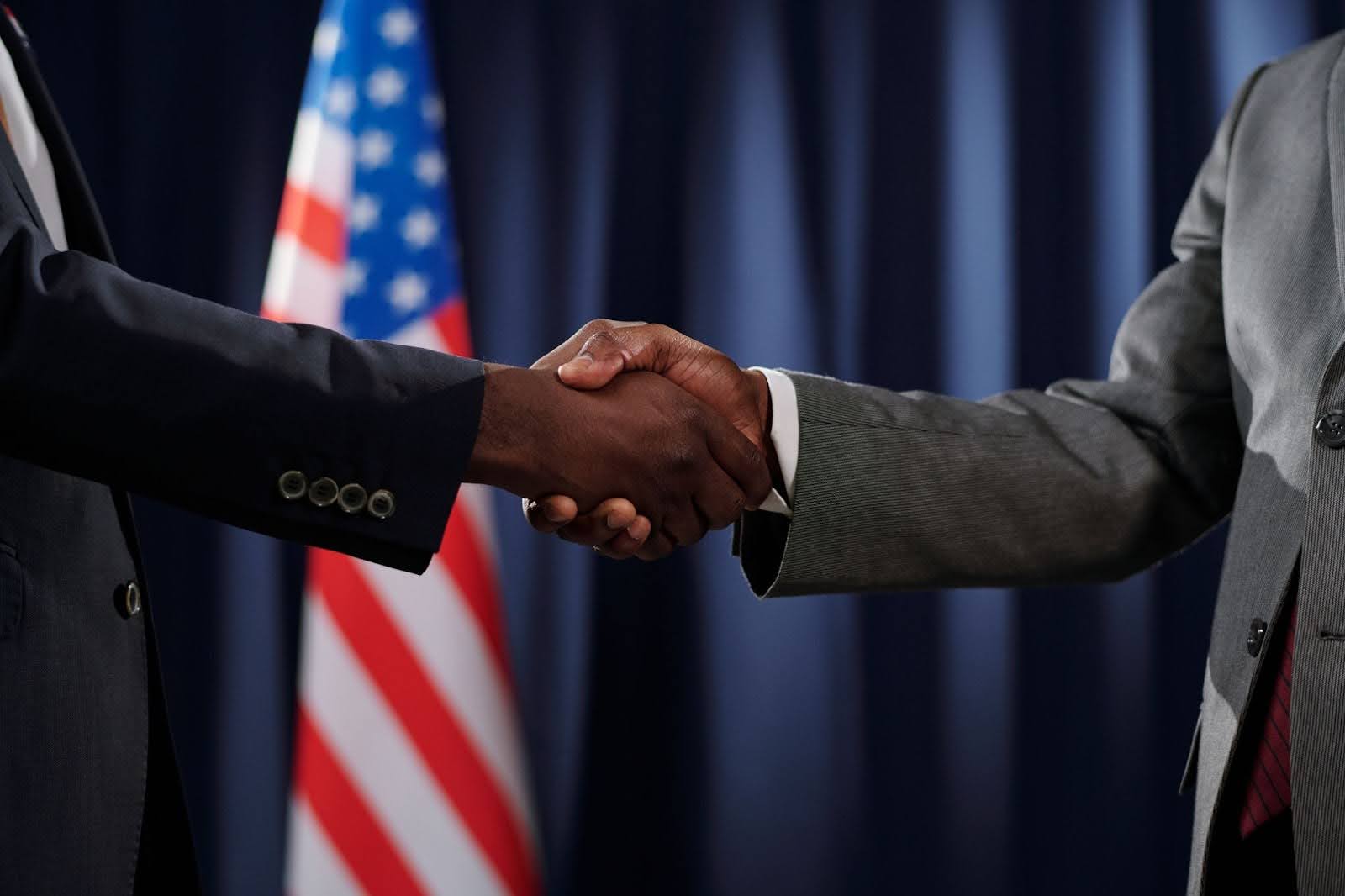Two men shaking hands with the US flag in the background