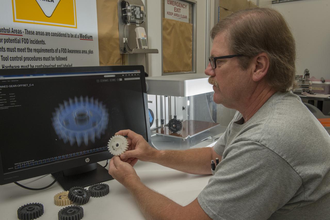 Phillip Steele (EM42/ESSSA) examines composite material gears printed with Marshall’s MarkForged® 3D Printer (background).