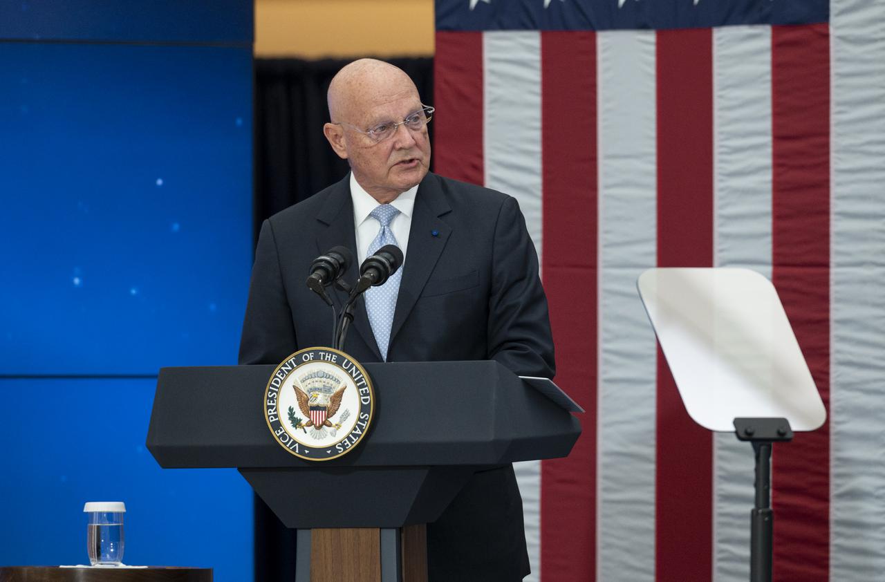 A US representative speaking on a stage with US flag in the background