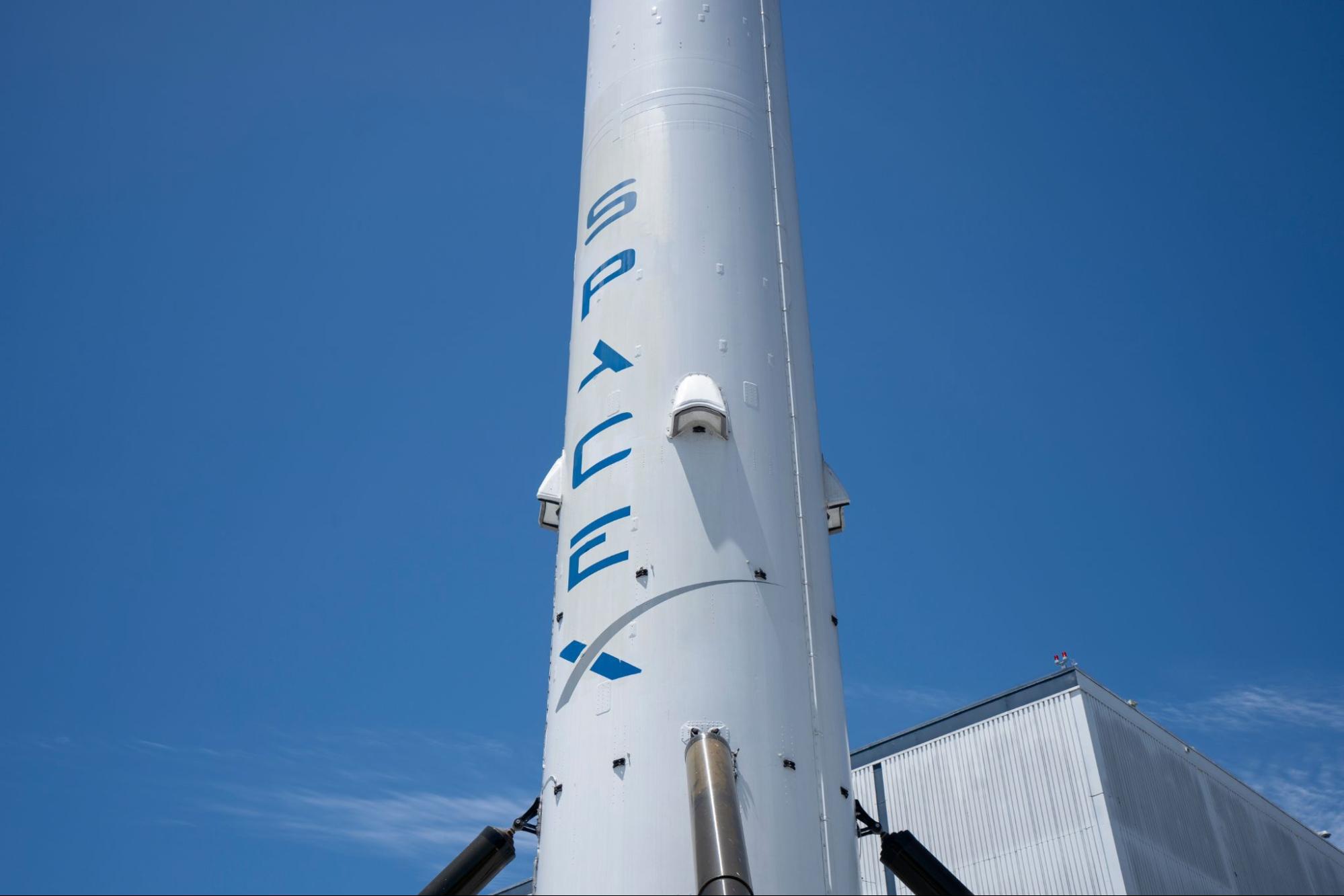 Close-up of a white rocket with "SPACEX" in blue, angled upwards against a clear blue sky.