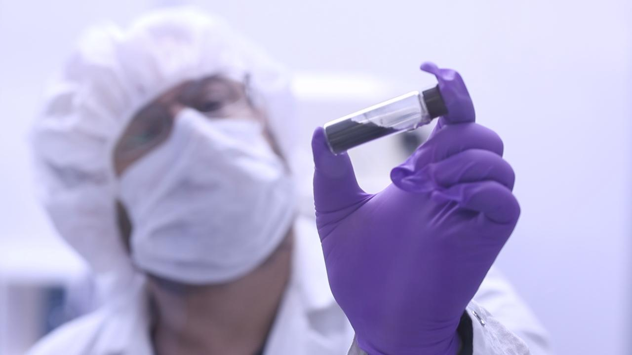 Scientist in white suit with purple gloves holding test tube.